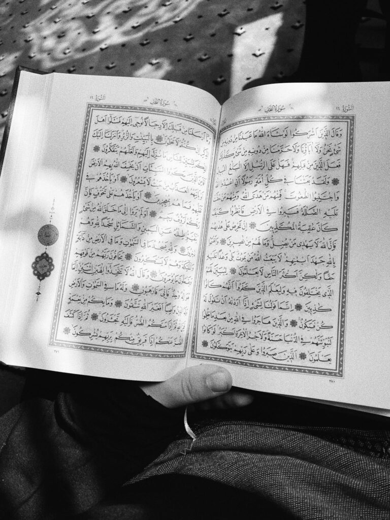 A black and white photo of an open Arabic book with sunlight casting shadows across the pages.