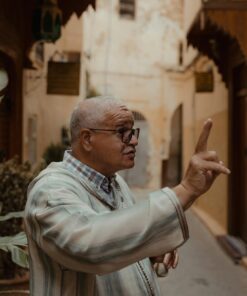 An adult man with glasses gestures while speaking in a historic street.