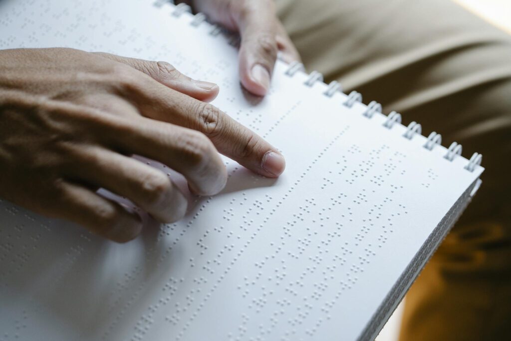 Close-up image of a person using fingers to read a braille book, highlighting tactile reading for the visually impaired.