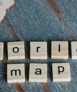 Close-up of Scrabble tiles spelling 'world map' on a textured wooden surface with map outlines.