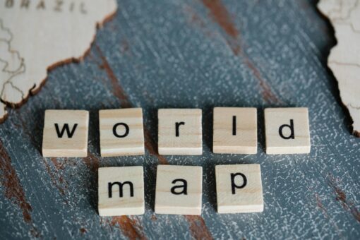 Close-up of Scrabble tiles spelling 'world map' on a textured wooden surface with map outlines.