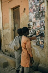 Two children examining colorful posters on a rustic urban street wall.