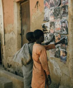 Two children examining colorful posters on a rustic urban street wall.