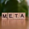 Wooden letter blocks spell META on a table with a blurred green background.