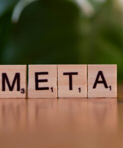 Wooden letter blocks spell META on a table with a blurred green background.